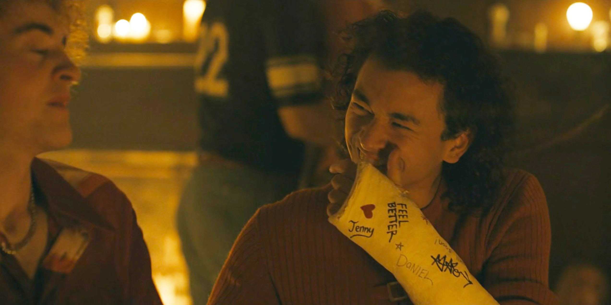 Character holding up a yellow signed arm cast with messages and drawings in Devil in Disguise E5