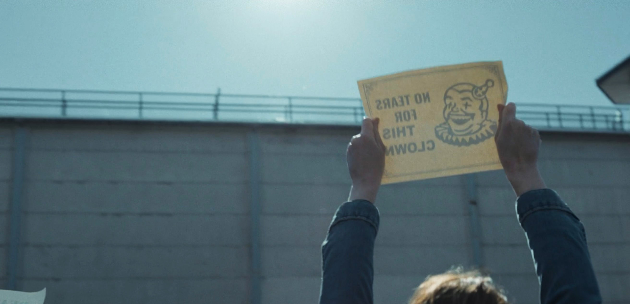 Protester holding up a No Tears For This Clown sign with clown illustration in Devil in Disguise E8