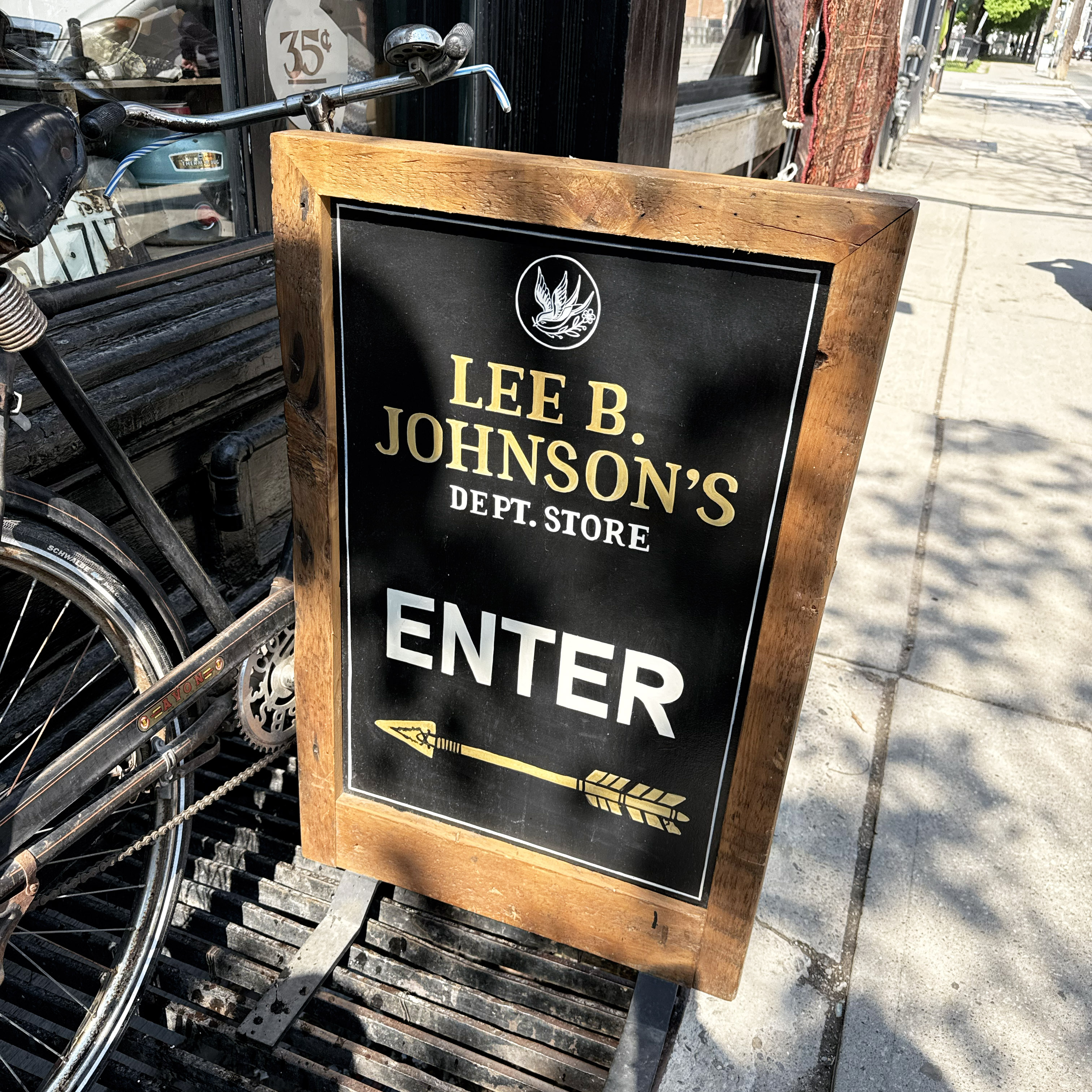 Lee B Johnson's sidewalk sandwich board sign with sparrow icon and gold-and-white lettering