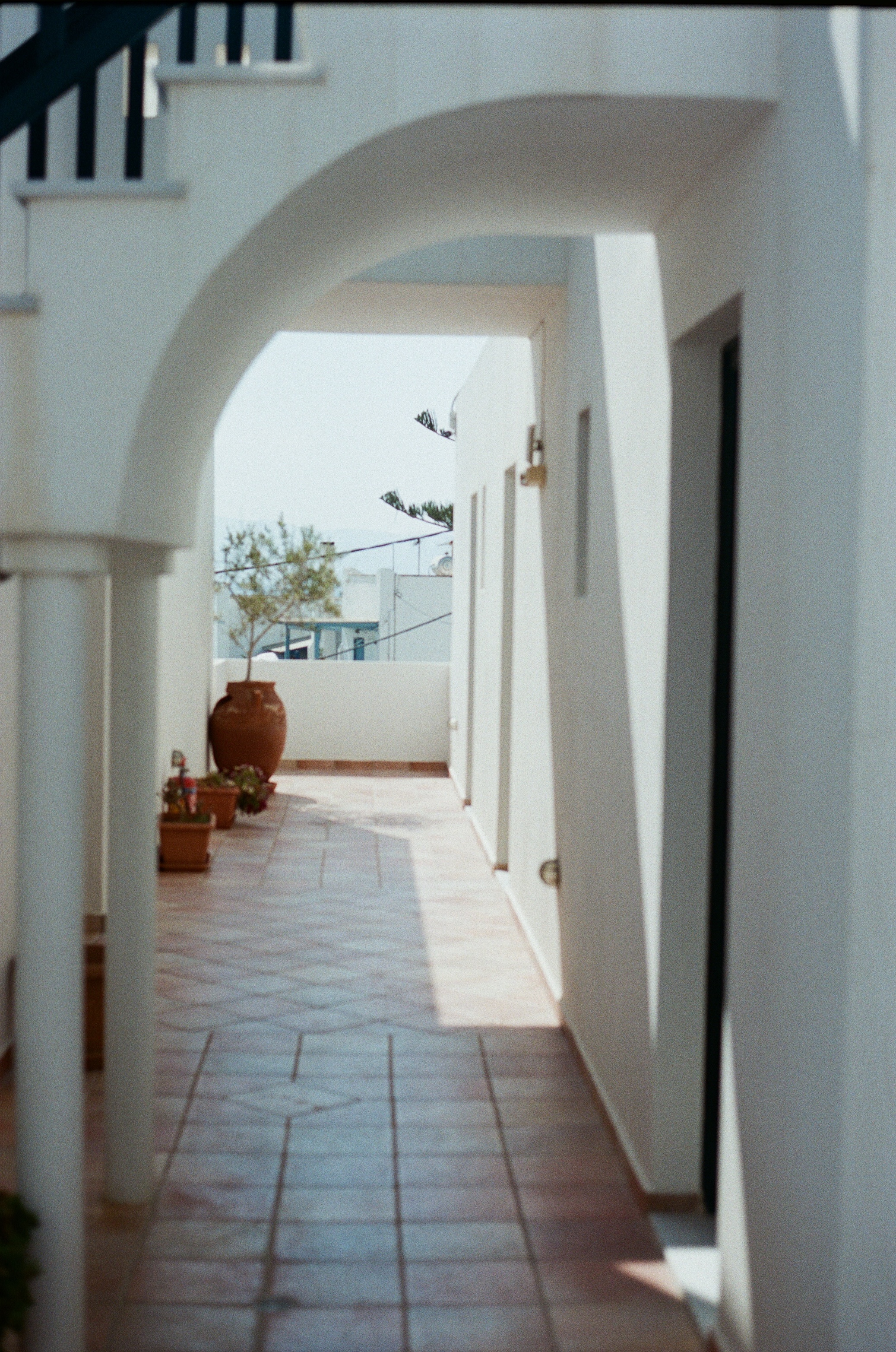 Whitewashed Greek terrace with archway, terracotta pots, and warm tile floor