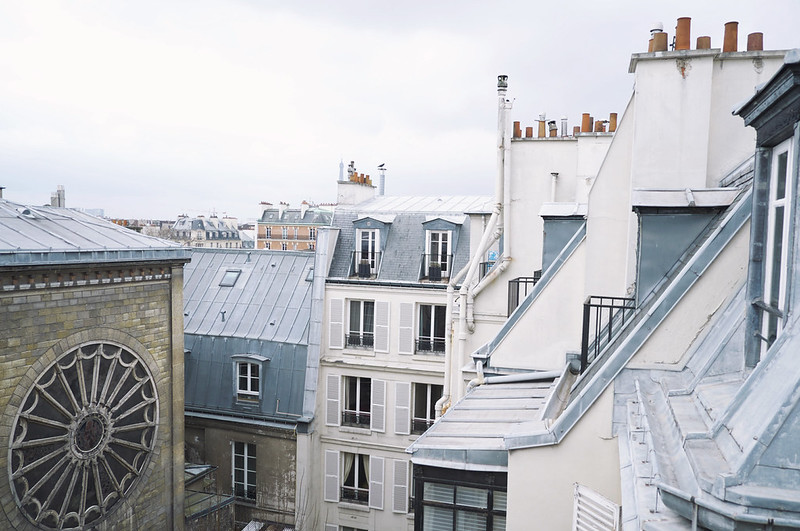 Parisian rooftops with zinc tiles and a rose window in soft grey light
