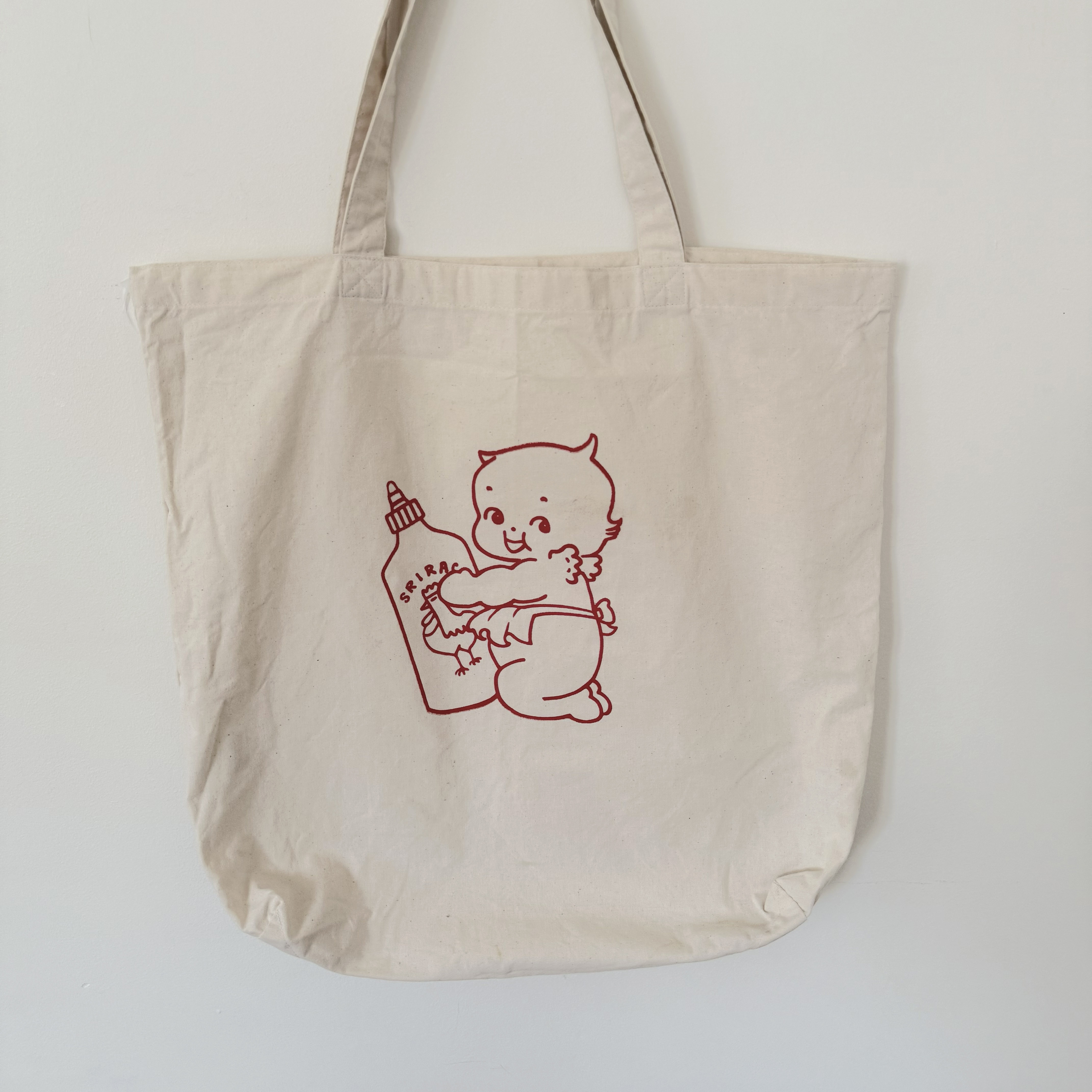 Hand-screenprinted Sriracha Kewpie design in red on a natural canvas tote bag