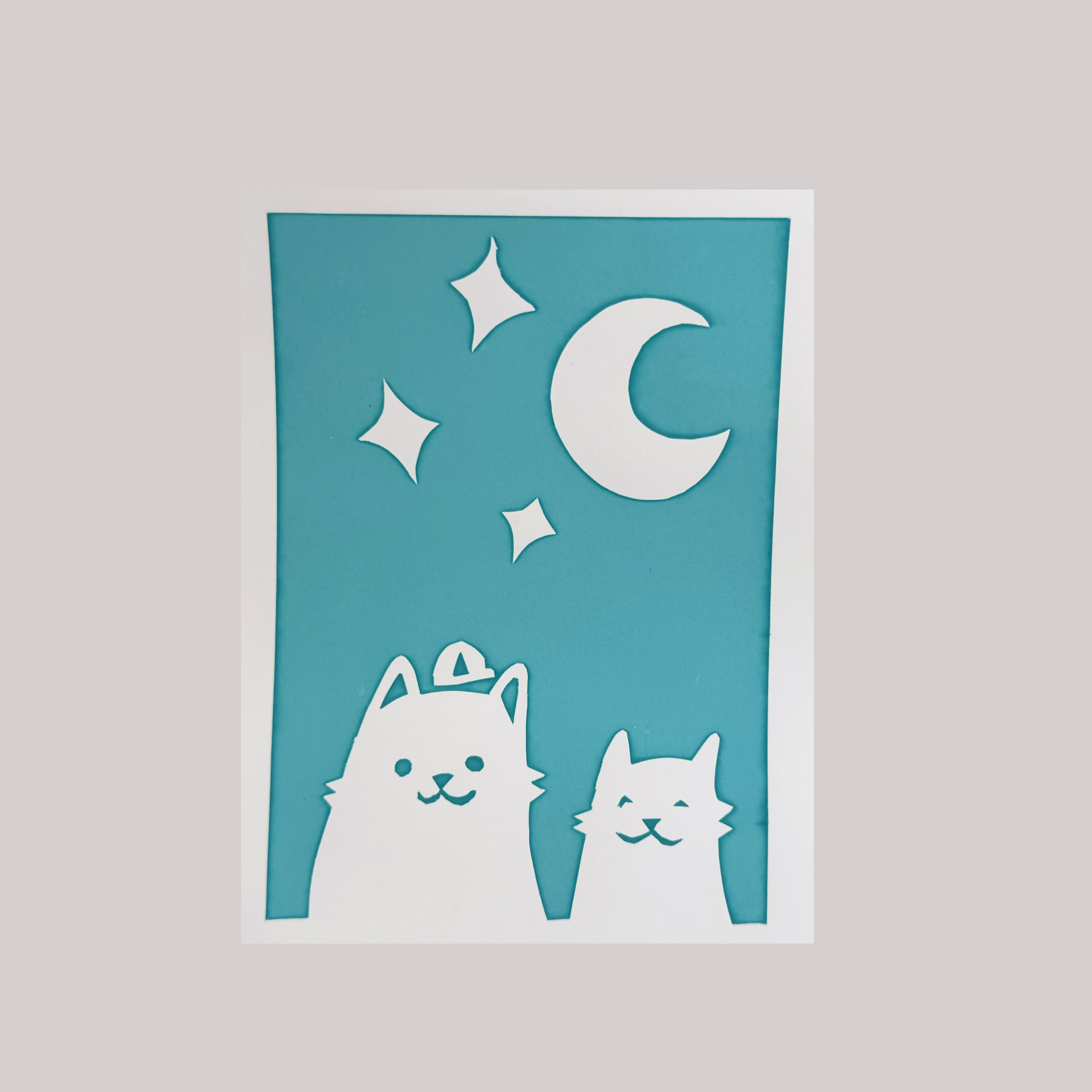 Teal and white papercut illustration of two cats under a crescent moon and stars