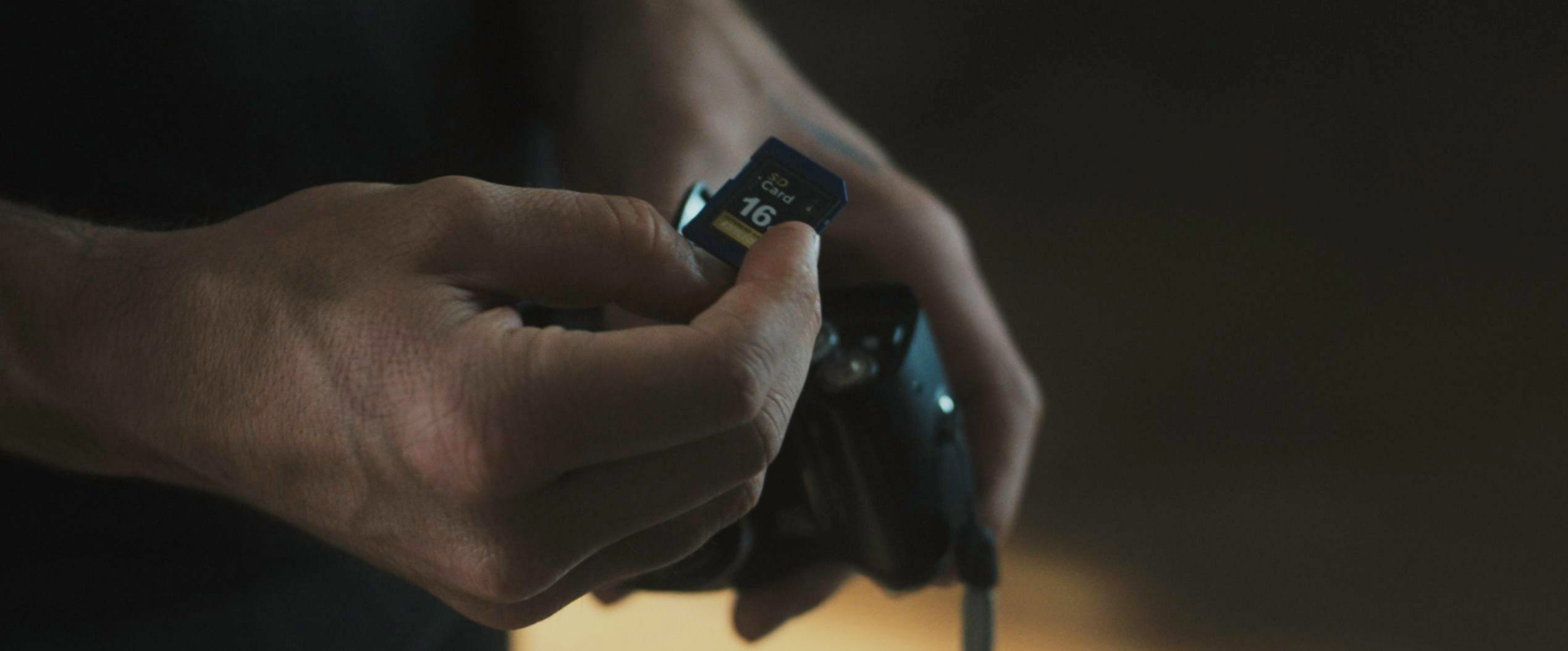 SD memory card with custom sticker held by Stephen in Tell Me Lies S3 E3