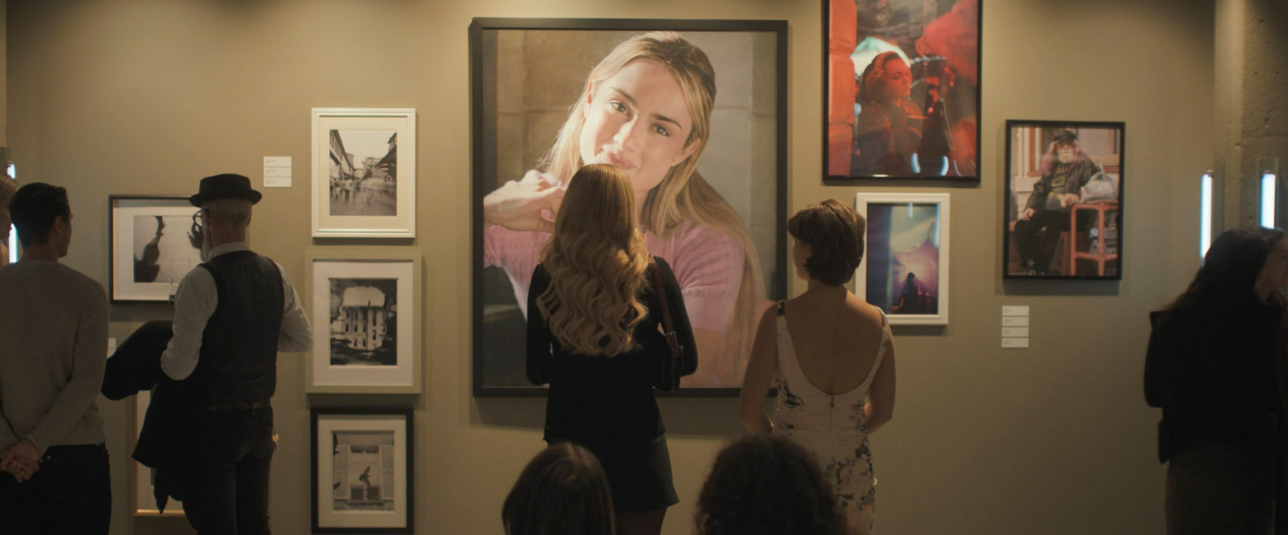 Art gallery scene with multiple framed photographs on the wall in Tell Me Lies S3 E7