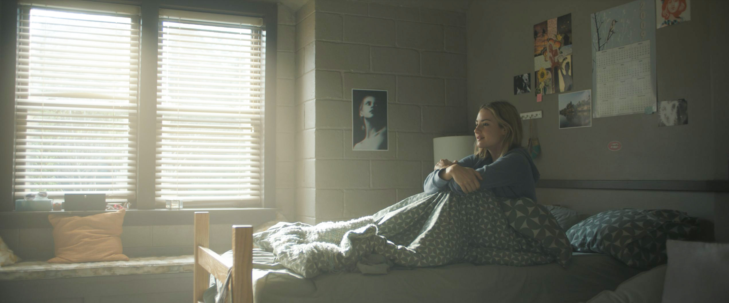 Lucy sitting on her bed with a custom poster on the wall behind her in Tell Me Lies S3 E8